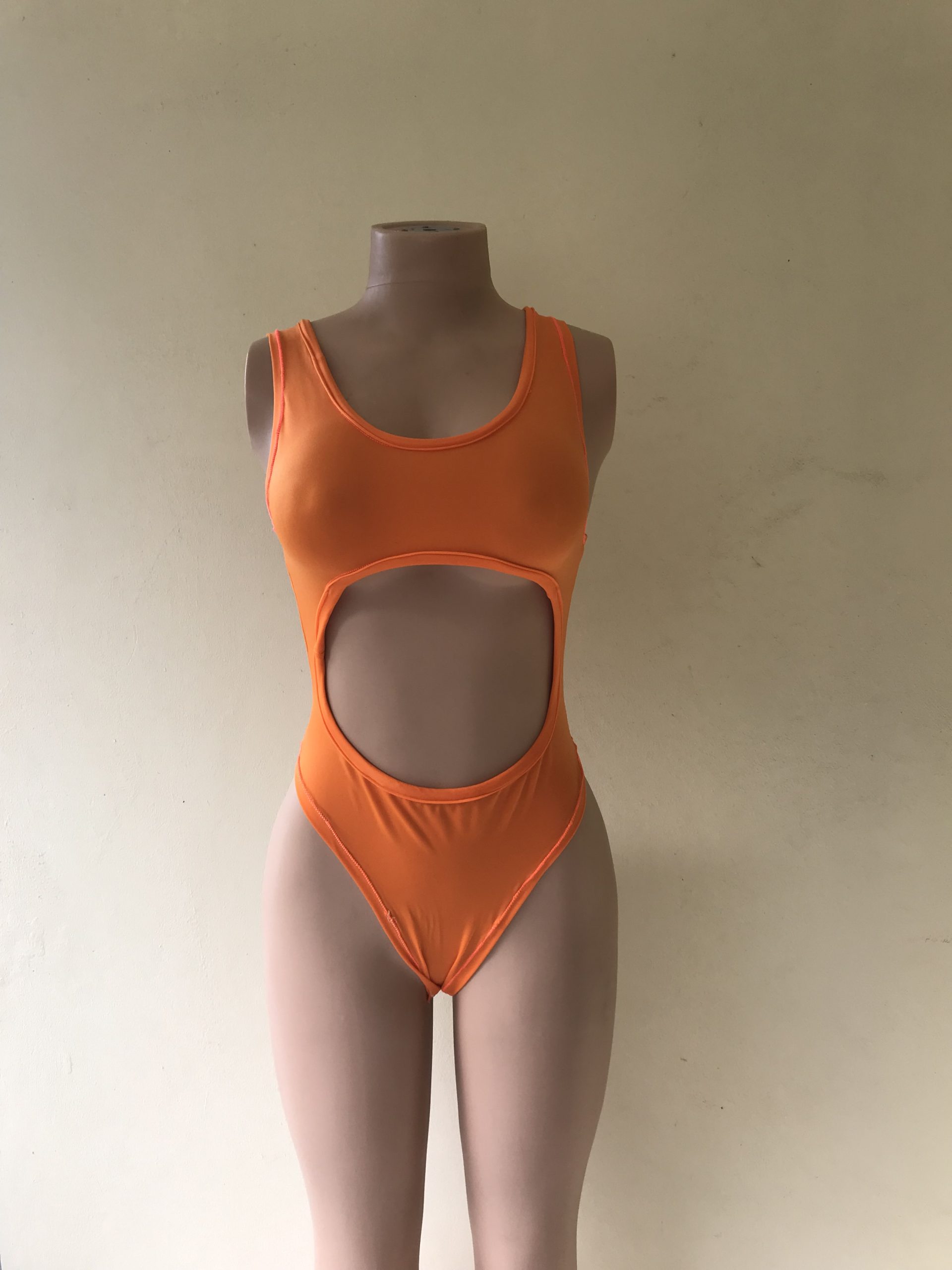 Temptress. A one-piece swimsuit in bright orange with bold midriff cut-out – front view on mannequin
