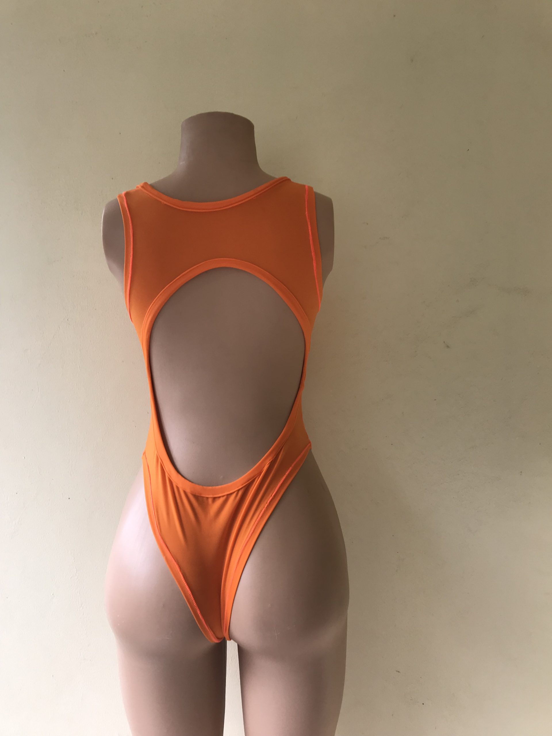 Temptress one-piece swimsuit in bright orange with open back and high-cut design – back view on mannequin